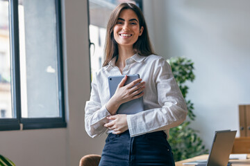 Beauty business woman using her digital tablet while looking at camera in a modern startup office