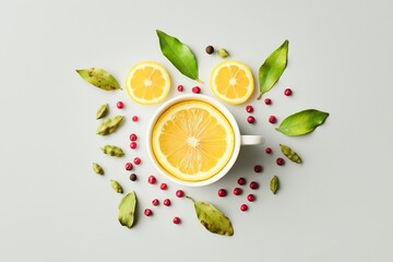 Arrangement of yellow lemon slices, cardamom, and pink peppercorns on a light gray background, with the elements forming an abstract shape resembling a cup or mug, with leaves as decoration. 