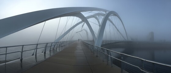 Obraz premium Misty morning on a modern pedestrian bridge. A lone figure walks into the fog.