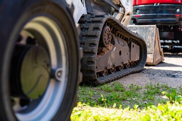 Heavy construction machinery rubber track and wheel on worksite with grass, industrial compact loader equipment for earthmoving, excavation and material handling tasks