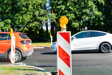 Cars passing road construction site with warning barriers and yellow lights in urban area during...