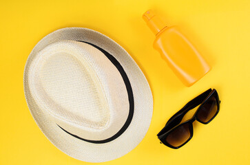 Summer straw hat sunscreen bottle and sunglasses on bright yellow background flat lay