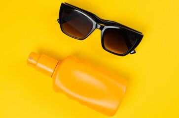 Sunscreen bottle and sunglasses on bright yellow background summer vacation concept