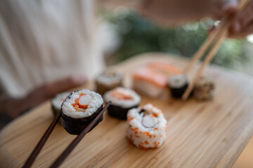 Woman picking up sushi roll with chopsticks from wooden board