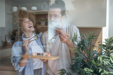 Happy couple eating sushi rolls with chopsticks at home