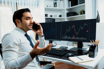 Trader businessman calling to consultant or partner with two stock exchange investment, compare...