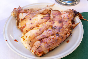 Thick slice of cheesy pizza with bacon and anchovies served on a white plate