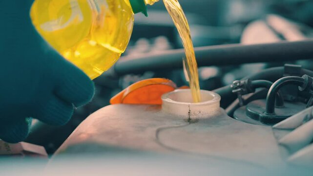 Car windshield washer fluid pouring into reservoir tank close up hands in blue work gloves refilling yellow cleaning liquid automotive maintenance