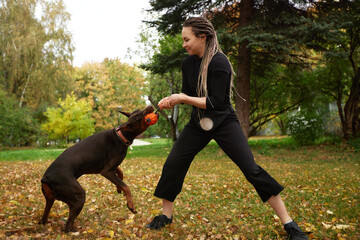 Woman playing tug-of-war with her dog in a vibrant autumn park
