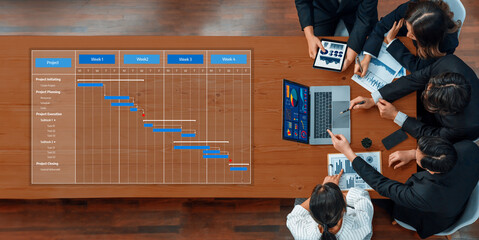 A group of professionals engaged in a project management meeting, analyzing a Gantt chart and...