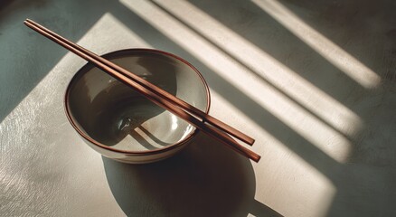 Serene Dining Scene with Chopsticks Resting on Bowl of Food in Soft Sunlight on Minimal Table Setting