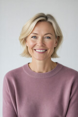 Obraz premium A smiling, middle-aged woman with blonde hair and a light pink sweater looks directly at the camera in a studio portrait.