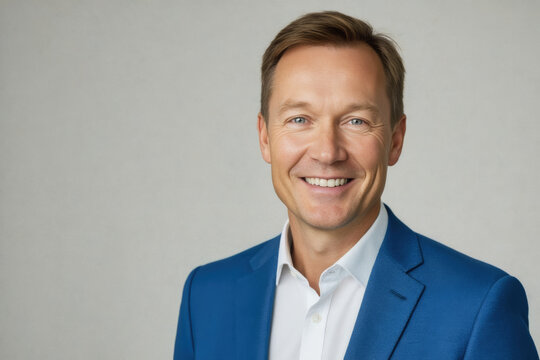 A smiling middle-aged man in a blue suit and white shirt poses confidently against a soft gray background.