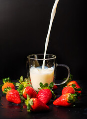 Strawberries and milk, a cup of milk surrounded by strawberries, black background, selective focus.