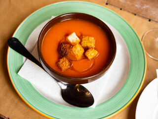 There is bowl with dinner dish on napkin-covered plate. Tender warm cream carrot soup of orange...