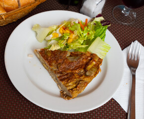 Slice of appetizing artichoke omelette served with colorful fresh vegetable salad and crusty bread. Traditional Spanish dish
