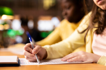 Multiethnic teens finishing their homework at a library after classes, engrossed in literature and...