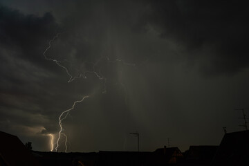 Dramatic thunderstorm illuminates the night sky over rooftops during a powerful lightning display