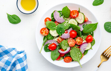 Healthy vegan vegetable salad with spinach, tomatoes, cucumber, onion, sesame seeds and olive oil. White table background, top view