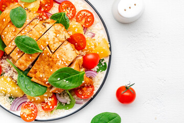 Yummy salad with chicken, couscous, tomatoes, onion, spinach and orange. White table background, top view