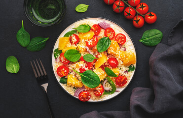 Gourmet vegan salad with couscous, tomatoes, onion, spinach and orange. Black background, top view