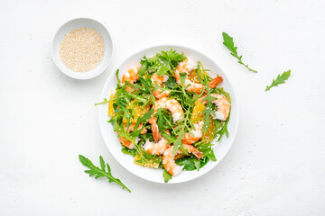 Delicious shrimp salad with juicy orange, fresh arugula and white sesame seeds on white plate, top...