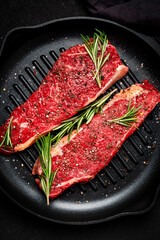 Raw beef sirloin steaks with rosemary, salt and pepper on grill pan. Black background, top view