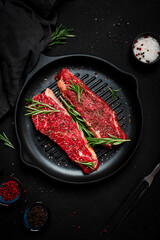 Raw beef sirloin steaks with rosemary, salt and pepper on grill pan. Black background, top view