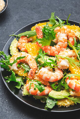 Seafood salad with shrimps, avocado, juicy orange, fresh arugula and sesame on black table, top view