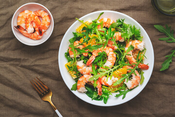 Delicious shrimp salad with juicy orange, fresh arugula and white sesame seeds on white plate, top view