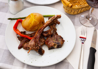 There are fried lamb ribs on plate. Meat appetizer is complemented with baked potatoes, bell...