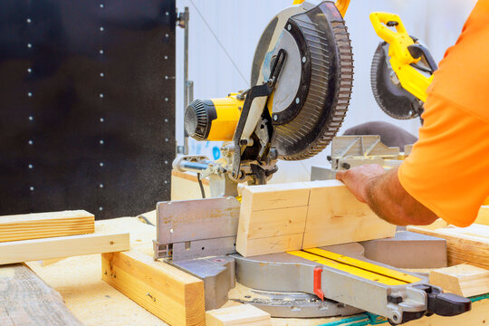 Skilled craftsman uses miter saw to precisely cut wooden boards in workshop filled with tools.