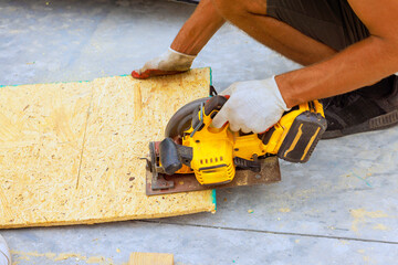 Contractor uses power saw to cut wood sheets at construction site on works day while wearing...
