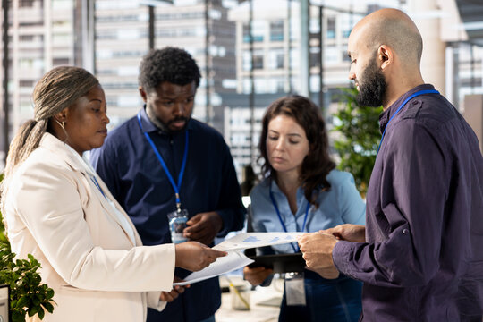 Multiethnic executive team meeting to discuss and look over administrative tasks, reviewing progress reports and corporate data to ensure alignment with company goals for effective management.