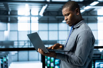 Engineer in data center operating laptop, deploying new server architectures, configuring network...