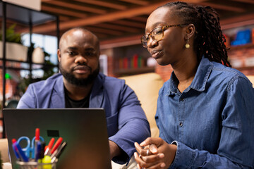 African american couple sitting on couch to share a business idea, using modern technology and...