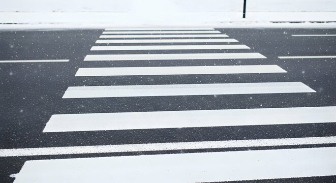 Snowy pedestrian crossing with white stripes on dark asphalt road minimal scenery