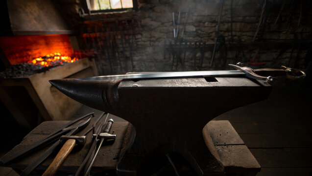 Atmospheric shot of a finished medieval sword resting on an anvil in a traditional blacksmith workshop with a glowing forge