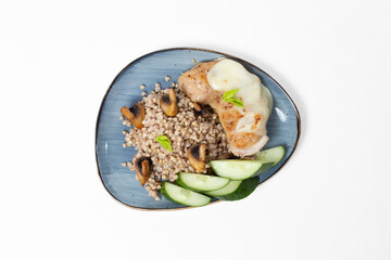 Buckwheat with sautéed mushrooms, baked chicken fillet topped with cheese, and fresh cucumber slices on a plate against a white background