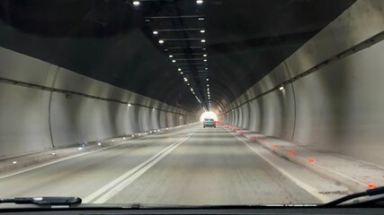 View from a car window while driving through a tunnel. The tunnel walls are illuminated by...