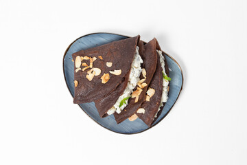 Chocolate crepes with cottage cheese filling and almond flakes on a plate against a white background
