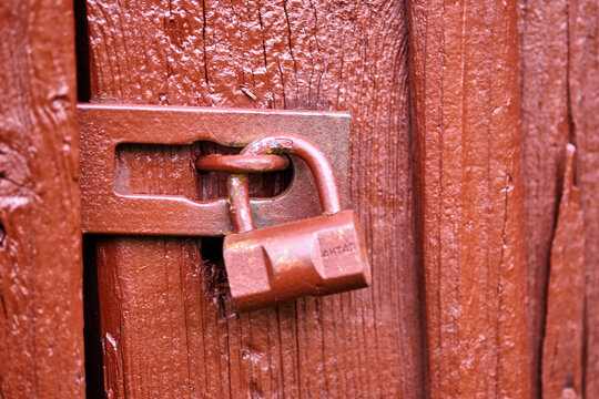 Rusty padlock securing a wooden door, showcasing details of weathered wood and metalwork on a quiet afternoon