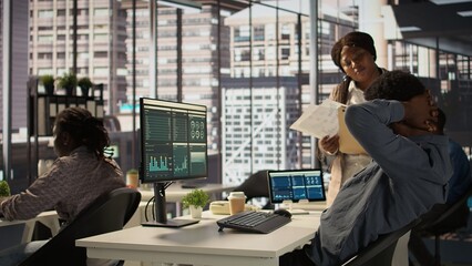 Black male CEO dealing with back pain and stretching his muscles at the desk, sitting with an...