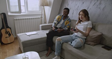 A diverse couple enjoys video games in their living room. The woman experiences frustration while gaming with her boyfriend. - Powered by Adobe