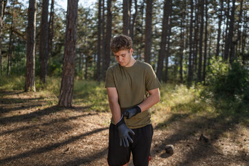 teenage man put gloves prepare to pick up waste garbage to clean forest