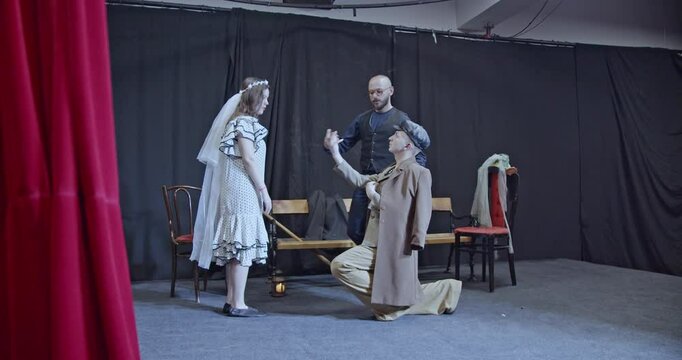 Young actors rehearse a scene on stage in a theater. A man proposes marriage and the director guides them.