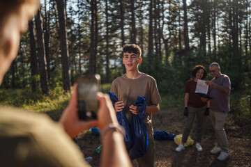 man filming friend volunteer activist in forest while hold plastic bags