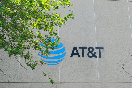 Cambridge, USA - 8 July 2025. AT&T logo on a beige wall of central office, partially covered by green tree branches on a sunny day.