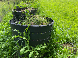 Black Plastic Compost Bins with Organic Garden Waste for Sustainable Recycling. Plastic containers filled with dry grass, weeds, food scraps, and vegetable waste for composting.