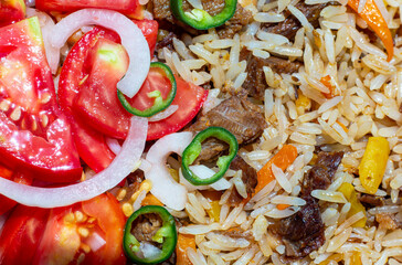 A close-up of pilaf garnished with a salad of chopped tomatoes, onions, and green chili peppers. This photo can be used in any food-themed design